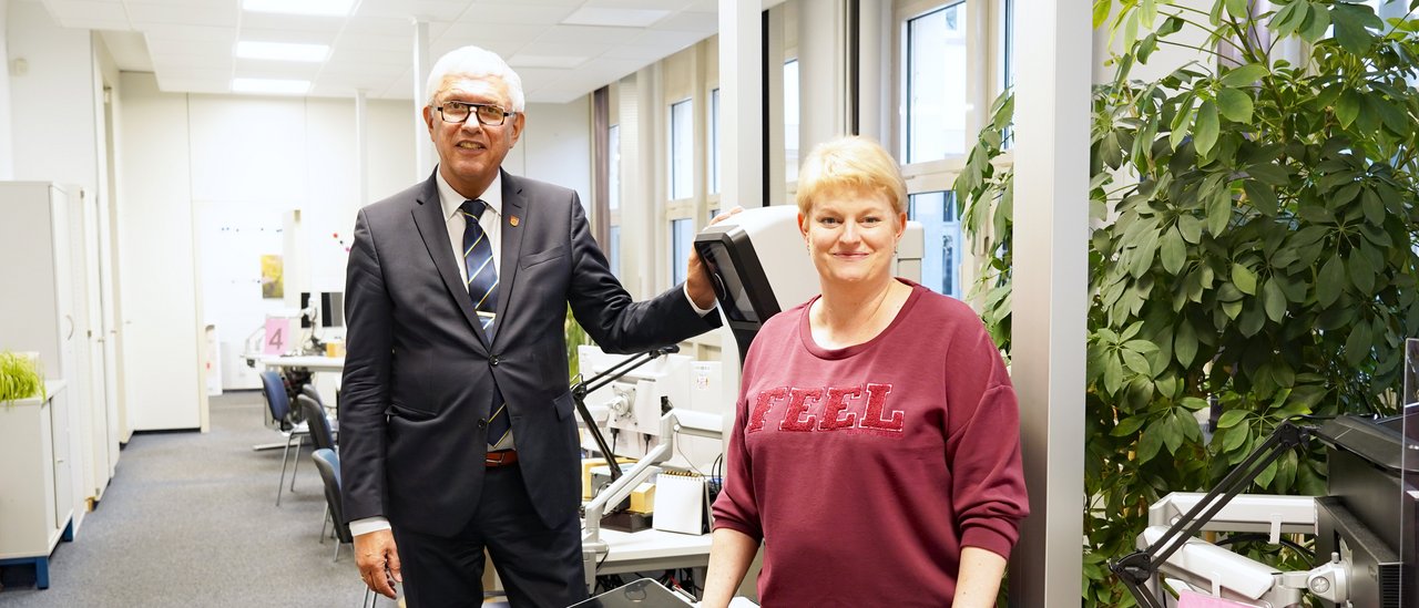 Bürgermeister Ralf Beßler und Monika Frauendorf aus den Bürgerservices stehen im Großraumbüro vor dem Passbildautomaten.