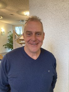 Peter Brücher im Foyer des Rathauses, lächelnd, kurze graue Haare und Pulli.