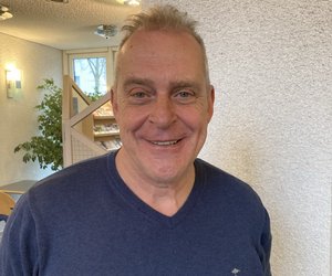Peter Brücher im Foyer des Rathauses, lächelnd, kurze graue Haare und Pulli.