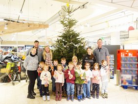 Kinder schmücken einen Weihnachtsbaum im Supermarkt.