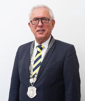 Bürgermeister Ralf Beßler, die Amtskette tragend, vor neutralem Hintergrund.