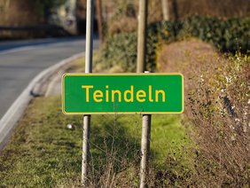 Hier ist das Schild der Ortslage Teindeln abgebildet, grün, mit gelbem Rand und Buchstaben.