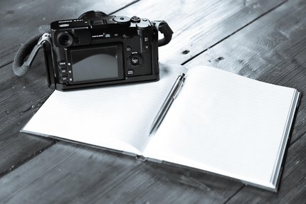 Bild eines Notizbuches und einer Kamera auf einem Tisch, als Symbolbild für Pressearbeit.