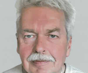 Portraitfoto von Peterdirk Schweighöfer, kürzere graue Haare, grauer Oberlippenbart, leicht lächelnd.