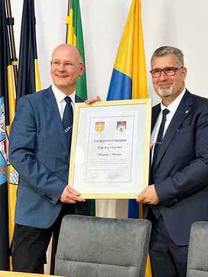 Die Bürgermeister Ulrich Schulte und Alexander Brodführer halten die Urkunde zur Erneuerung der Städtepartnerschaft hoch.