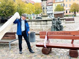 Bürgermeister Ulrich Schulte enthüllt eine Bank aus Holz, die mit einem weißen Tuch abgedeckt war.