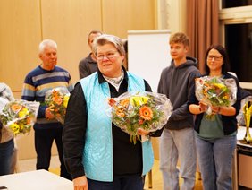 Sportabzeichenobfrau Uta Wiele wird unter Applaus verabschiedet, sie hält einen Blumenstrauß und lächelt.