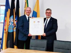 Die Bürgermeister Ulrich Schulte und Alexander Brodführer halten die Urkunde zur Erneuerung der Städtepartnerschaft hoch.