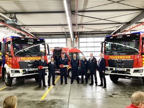 Drei neue Feuerwehrfahrzeuge in der Halle, davor die Akteure von Feuerwehr und Stadtverwaltung.