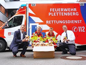 Bild von der Übergabe der Notfallbären durch die Sparkasse, vor einem Rettungswagen knien vier Personen.
