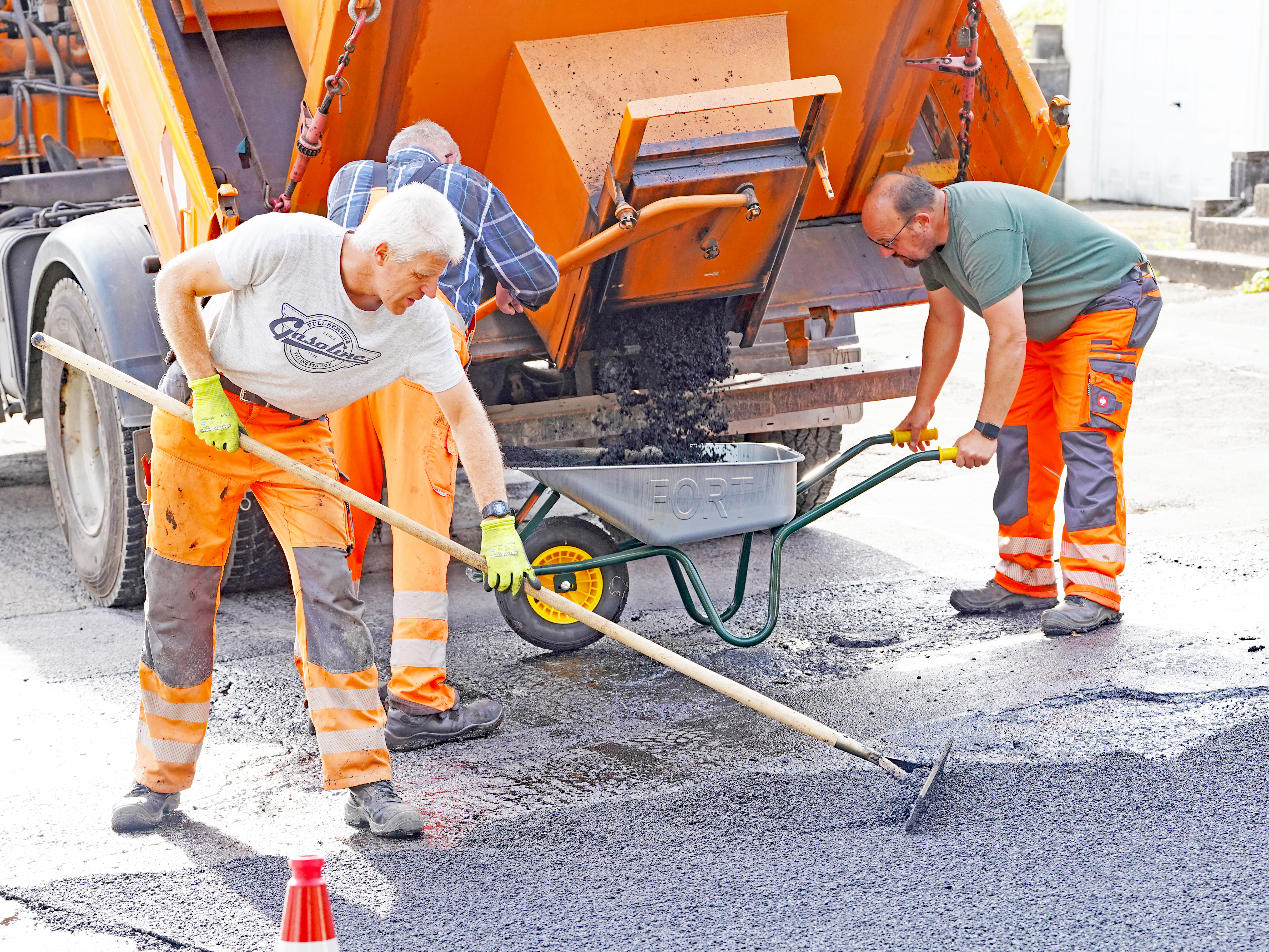 Mitarbeiter verteilen den Asphaltbeton aus der Schubkarre. (Bild: Stadt Plettenberg)